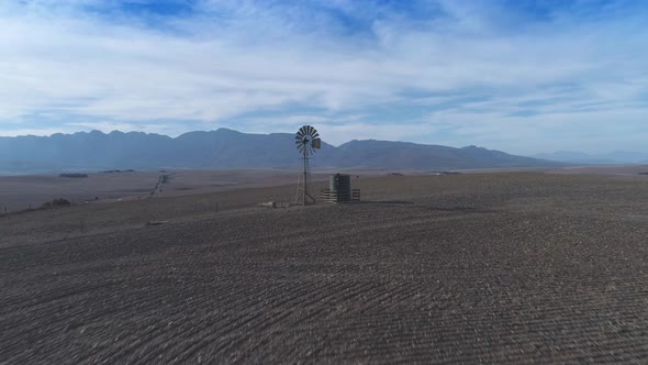 Drone flies over dry farm land and turning windpump during dry summer.