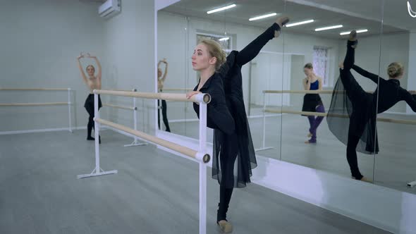 Elegant Beautiful Ballerina Rehearsing Arabesque in Dance Studio with Ballet Dancers at Background