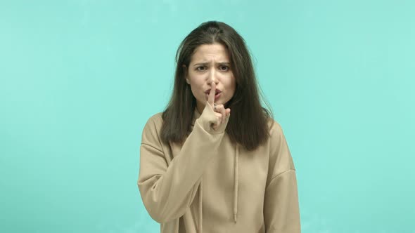 Angry Young Woman in Beige Hoodie Staring Annoyed and Showing Hush Sign Telling to Shut Up Be Quiet
