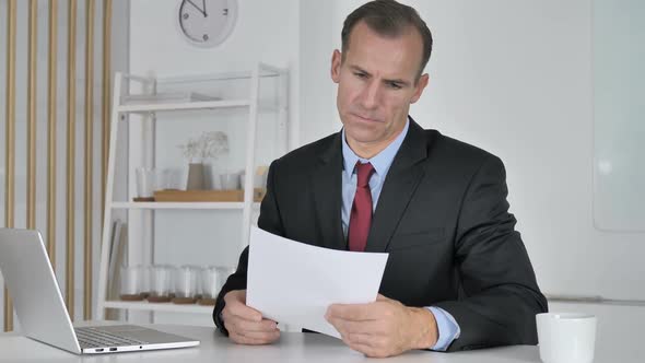 Angry Middle Aged Businessman Reacting to Loss While Reading Documents