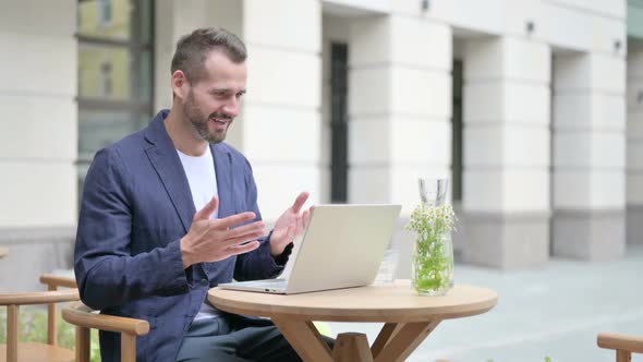 Man Celebrating While Using Laptop Sitting in Outdoor Cafe on Bench