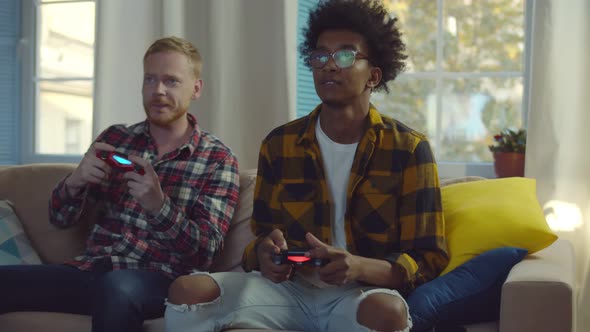 Smiling Diverse Male Friends with Gamepads Playing Video Game at Home