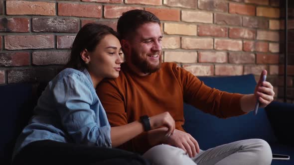 Cheerful Young Couple Waving Hands and Greeting in Mobile Phone Video Call Online Sitting Together