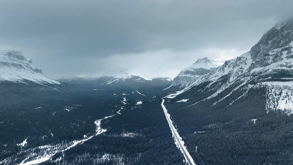 Drone captures the mountain peaks contrasting with the dark, dense forest below in Alberta, Canada