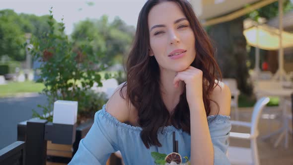 Beauiful Woman Sitting in Outdoor Restaurant and Sip Mojito Dring in Summer Hot Day