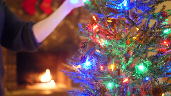 Decorating a christmas tree  with colorful festive lights, ornaments and stockings over the fireplac