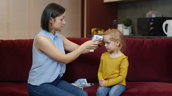 Mother Measures Temperature with Contactless Digital Thermometer of Her Sick Daughter Child at Home