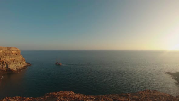 Sunset in Tiritaña Beach, Gran Canaria, Spain, with a boat sailing and blue sky framed by high cliff