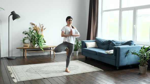 Lovely adult woman doing yoga asanas while standing in the room. Yoga classes at home
