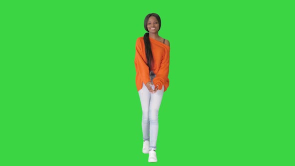 Smiling African American Woman Dressed in Bright Sweater and Jeans Walking Touching Her Hair