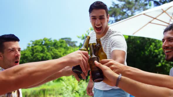 Group of happy friends toasting beer bottles at outdoors barbecue party