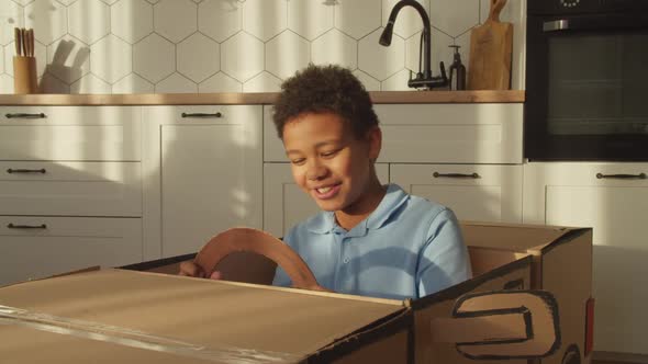 Portrait of Carefree Preadolescent Black Kid Playing Driving Toy Cardboard Car