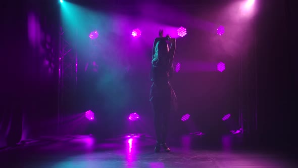 A Young Woman in a Black Short Dress Is Dancing Rumba Elements Against a Background of Purple Lights