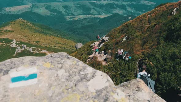 Group of Tourists and Children with Backpacks Go Down on Stone Trail in Mountain