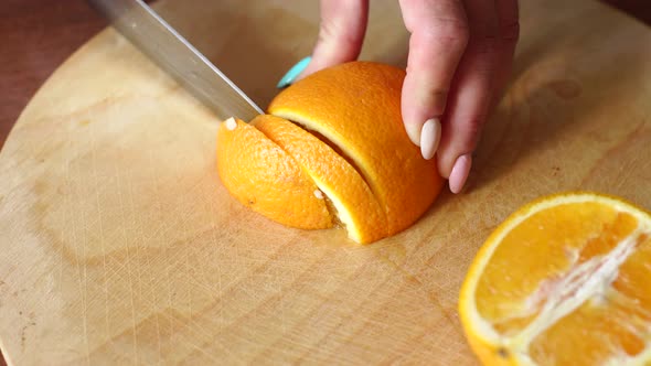 Closeup Girl Cuts a Ripe Juicy Orange on a Wooden Board