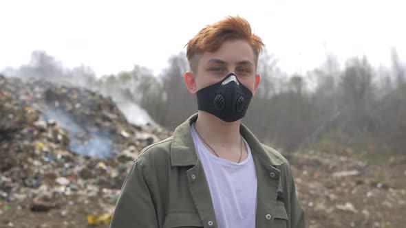 Portrait of young guy in a medical mask looks at camera on huge plastic landfill background