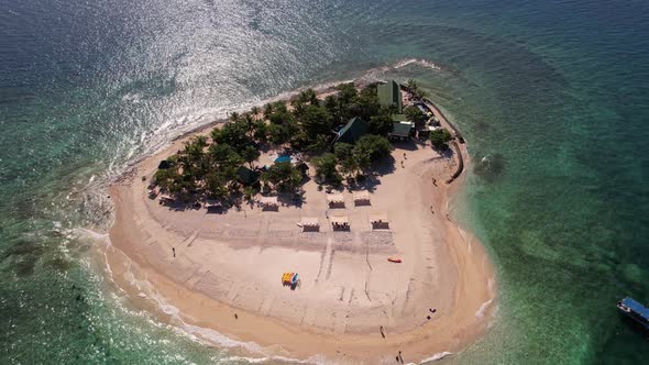 Static drone looking down on a small tropical island as people walk around and small waves crash ont