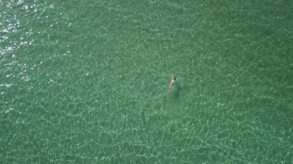 Rotating drone shot of a beautiful woman swimming on her back in the Aegean Sea; Paros island, Greec