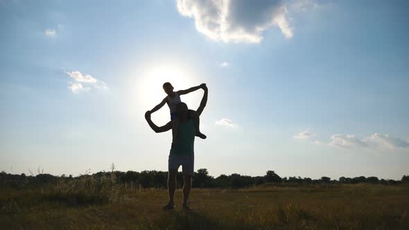 Happy Father Holding His Little Son on Shoulders and Walking at Meadow on Sunny Summer Day