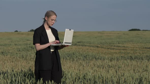 employee of an agricultural firm with a laptop checks the quality of wheat in the field