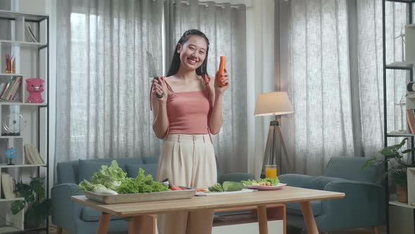 Smiling Asian Woman Holding A Knife And Slicing Carrot Before Posing To Camera At Home