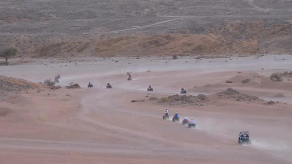 Group on Quad Bike Rides Through the Desert in Egypt on Backdrop of Mountains