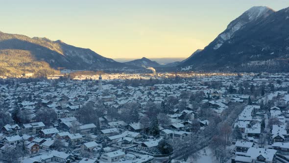 Snowy Garmisch-Partenkirchen town in shadow of mountains, drone shot.