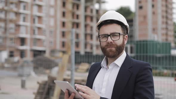 Portrait of Young Businessman with Tablet on Construction Site Looking To Camera Wearing a Safety