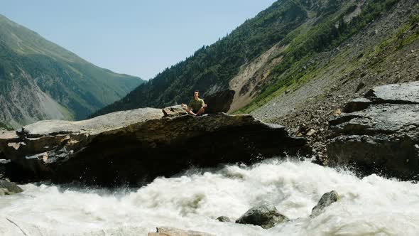 Man Sits in a Lotus Position and Meditates in Mountains River Flows Fast