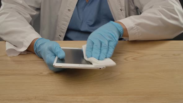 Prevention of COVID-19. A Man in a Protective Medical Suit Wipes a Tablet with an Antibacterial