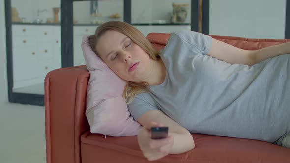 Bored Woman Lying on Sofa and Changing Tv Channels with Remote Control at Home