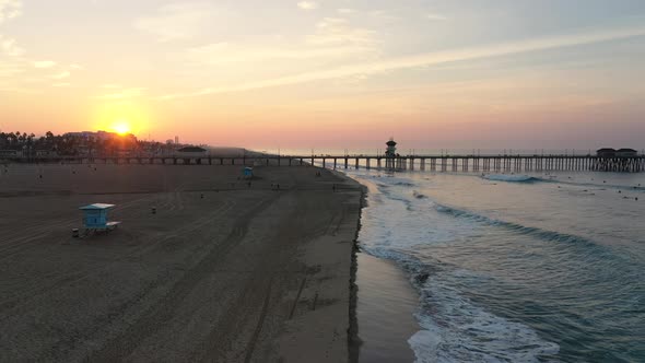 A stunning 4k view of the pier at sunrise, waves crashing , and surfers surfing in Surf City Califor