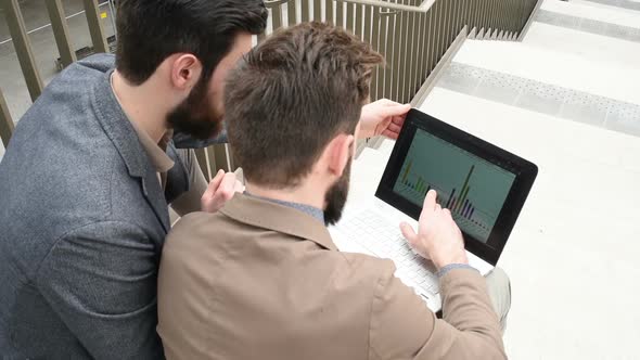 two young bearded men from behind sitting outdoor using personal computer