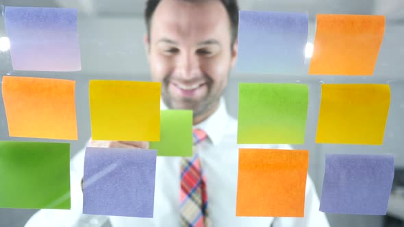 Businessman Working On Sticky Notes Attached on Glass in Office