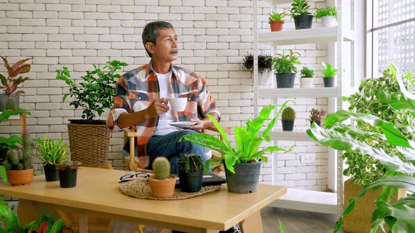 An old man sitting in a living room decorated with flower pots.