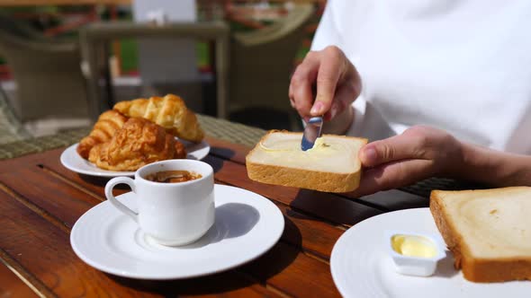 Hand Spreading Butter On Toast Having Breakfast With Coffee And Croissants.