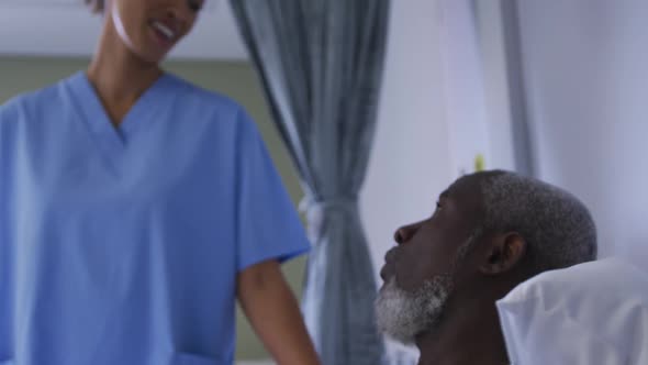 African american male patient in hospital bed talking with mixed race female doctor