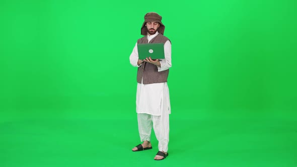 A Man of Arab Appearance in Traditional Clothes Uses a Laptop to Surf the Internet While Stands