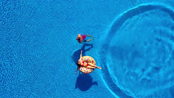 Aerial View of Man Dives Into the the Pool While Girl Is Lying on a Donut Pool Float