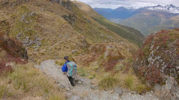 Tilt up, hiker descends exposed alpine pass, Routeburn Track New Zealand