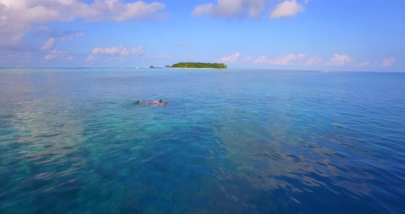 Aerial drone view of a man and woman couple snorkeling over the coral reef of a tropical island