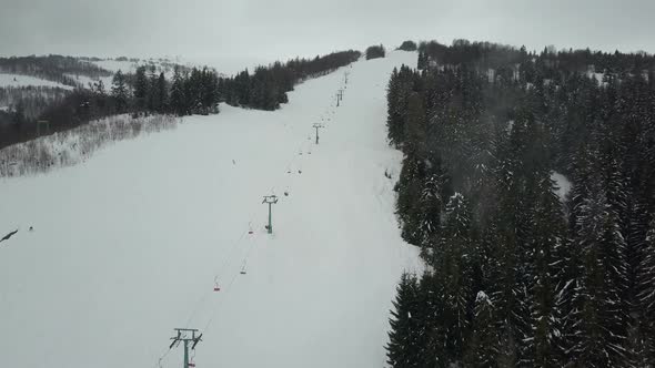 Flight Over a Ski Lift in Carpathian Mountains. Aerial View of People Descending on Skis