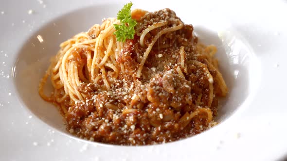 Chef Sprinkles Parmesan on Pasta Bolognese on White Plate in Restaurant