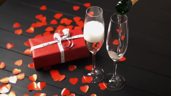 Champagne Is Filled Into a Glass on a Black Table Near a Gift Box.