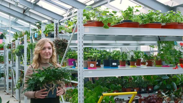 A Woman with Blond Hair Holds a Flowerpot of the Fern Family in Her Hands