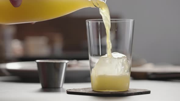 Slow Motion Man Pour Orange Soda Over Ice in Tumbler Glass to Make Spritz Drink on Concrete