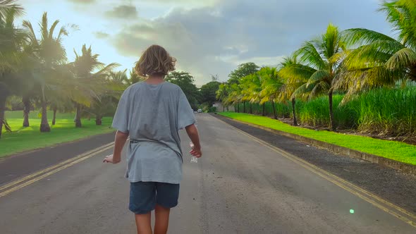 A Teenager Rides a Longboard Along a Beautiful Road with Green Palm Trees