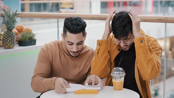 Two Young Indian Guys Students Sitting in Cafe Get Paper Letter Shocked Surprised Happy Men Reading