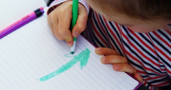 Cute schoolgirl drawing pictures in classroom