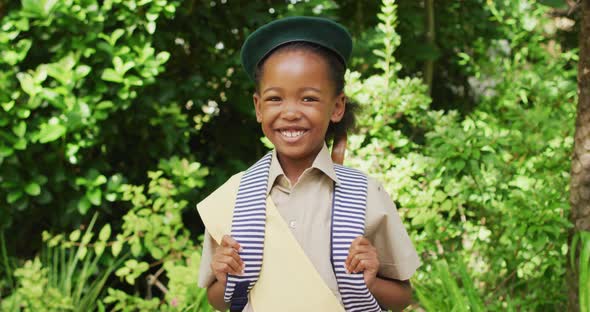 Animation of african american girl in scout costume smiling at camera in garden